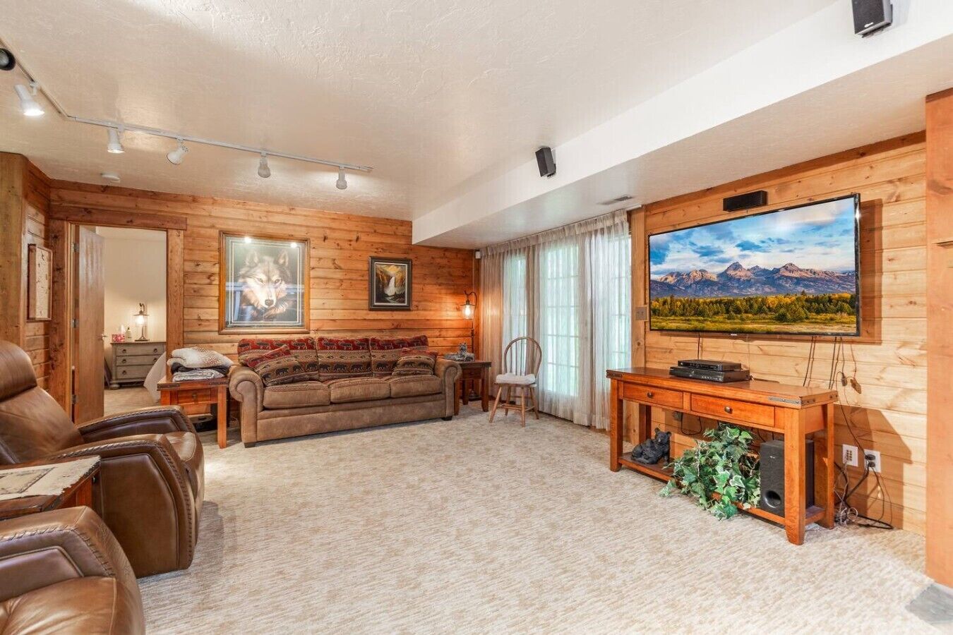 A cozy living room with a wooden interior, a large flat-screen TV, a sofa, and leather chairs.