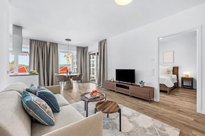 A modern living room with a sofa, coffee table, TV, and dining area.