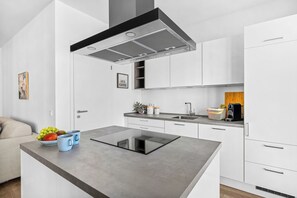 Cuina moderna amb armaris blancs, una placa vitroceràmica negra i una campana extractora d'acer inoxidable.