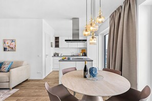 A modern kitchen with white cabinets, a dining area with a round table, and a living room with a sofa. - "Küstenglück" Luxury Rental – Baltic Sea Vacations with Ocean Views (Lübeck)