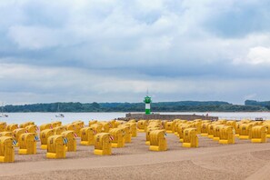Ein Strand mit gelben Briefkästen, die in Reihen angeordnet sind, ein Leuchtturm im Hintergrund und ein Gewässer mit Booten.
