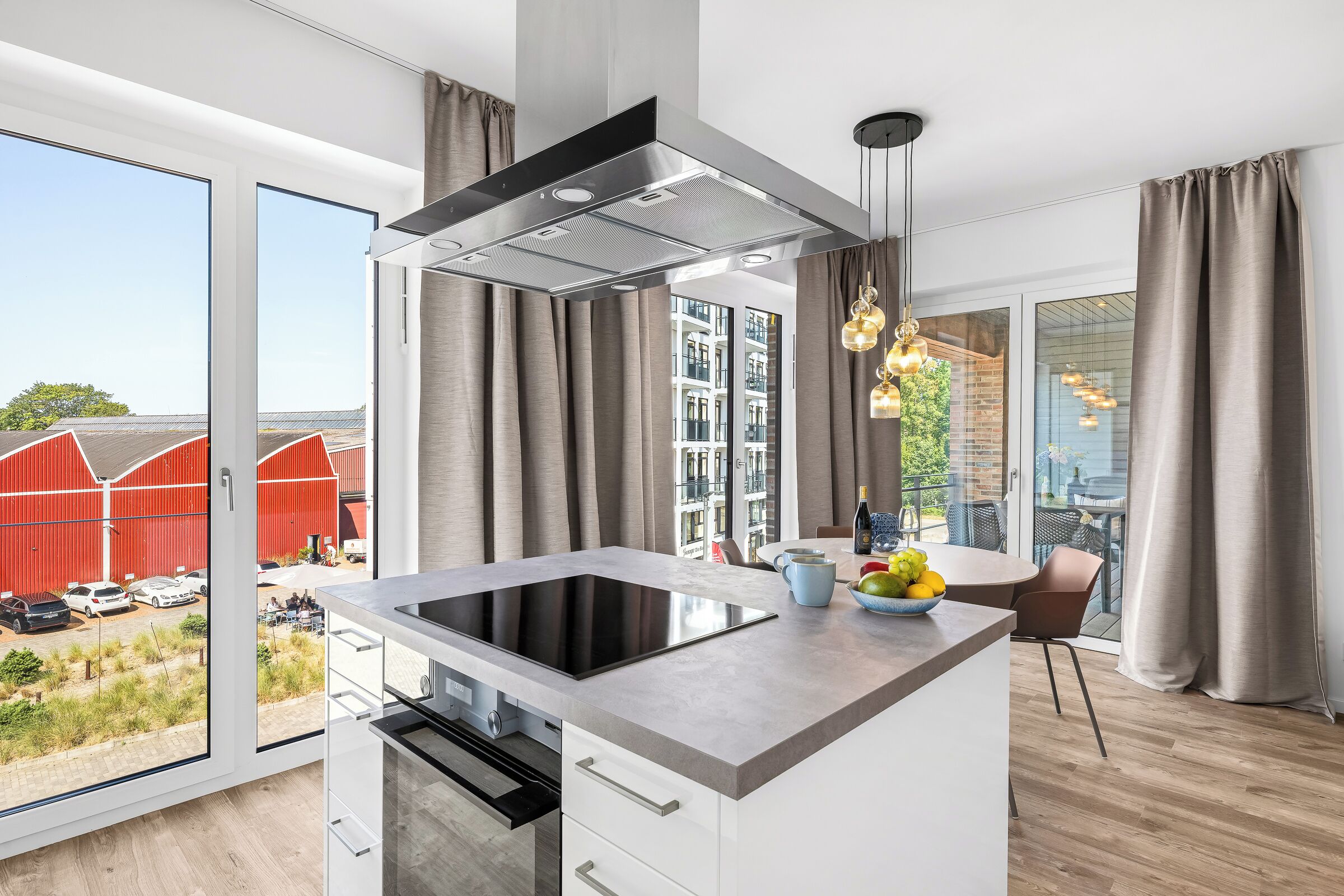 Eine moderne Küche mit einer zentralen Kochinsel, einem eingebauten Backofen und einem großen Fenster mit Blick auf einen roten Bauernhof und Grünflächen.