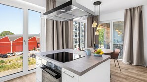 Une cuisine moderne dotée d’un îlot central, d’un four encastré et d’une grande fenêtre donnant sur une grange rouge et un paysage verdoyant.
