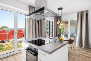 Eine moderne Küche mit einer zentralen Kochinsel, einem eingebauten Backofen und einem großen Fenster mit Blick auf einen roten Bauernhof und Grünflächen.