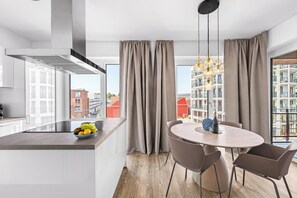 A modern kitchen with a large window, a dining area with a round table and chairs, and a view of buildings outside. - "Küstenglück" Luxury Rental – Baltic Sea Vacations with Ocean Views (Lübeck)