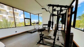Een sportschool met trainingsapparatuur, grote ramen en uitzicht op een woongebied.