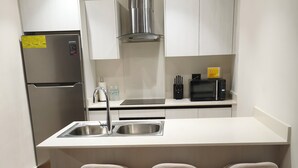 Een moderne keuken met een roestvrijstalen koelkast, een magnetron en een inbouwoven. Er staan drie barkrukken bij het eiland en een spoelbak met een kraan.