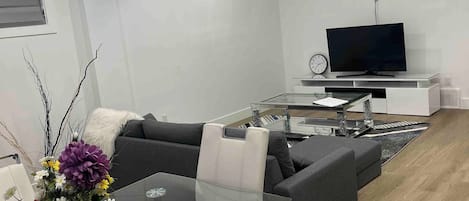 Ein modernes Wohnzimmer mit einem Glastisch, einer Couch, einem Fernseher und einer dekorativen Vase mit Blumen.