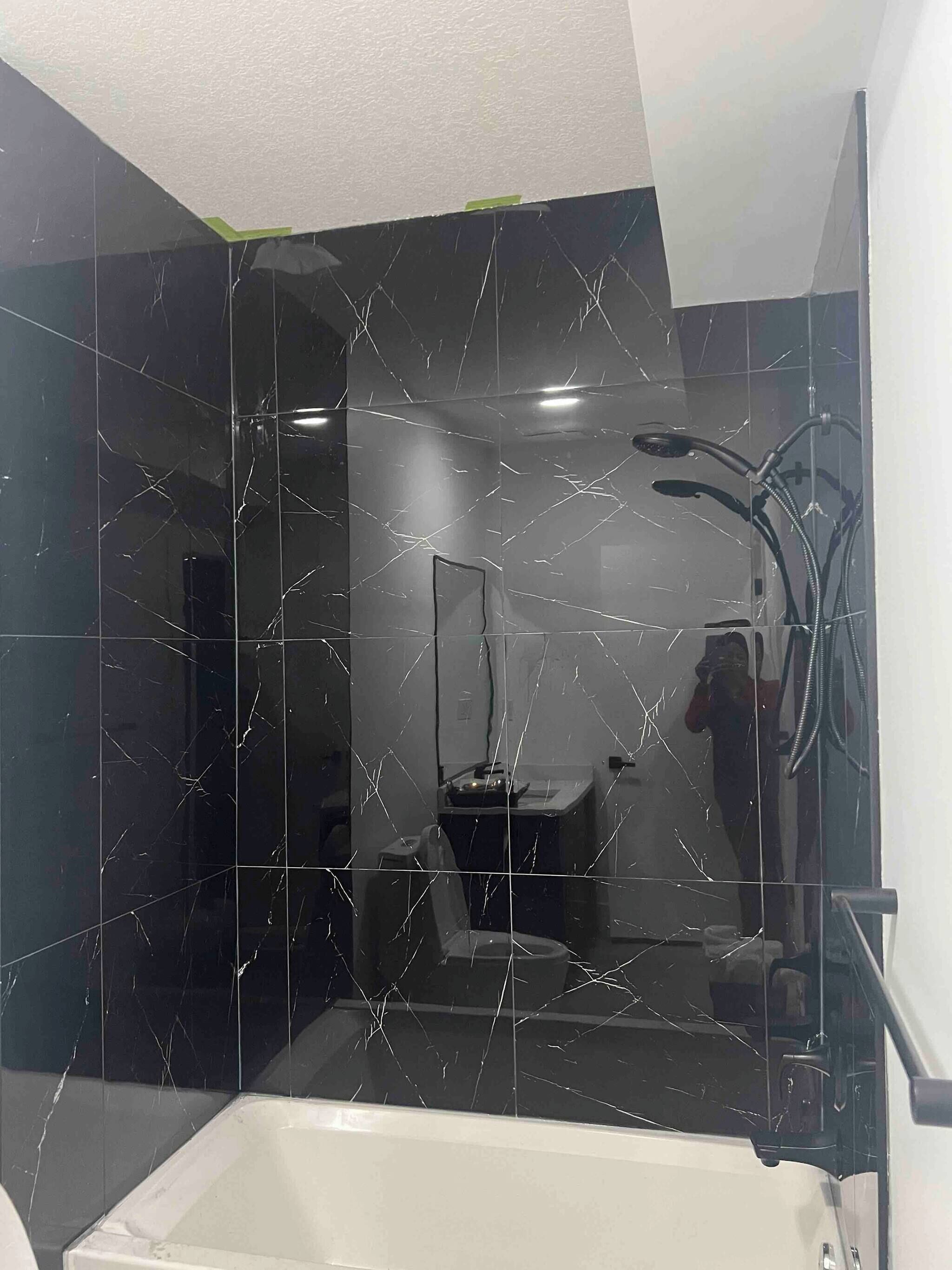 A bathroom with a black marble wall, a white bathtub, and a shower area.