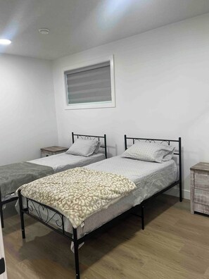 A room with two single beds, a window with blinds, a small bedside table, and a wooden floor. - Room-magnificent Brand New Luxurious Bas (Edmonton)