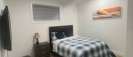 Une chambre à coucher avec un lit, une table de chevet, une lampe, un téléviseur et un tableau au mur.