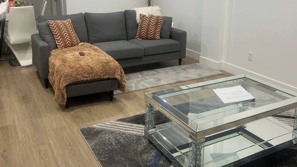 A modern living room with a grey sofa, a glass coffee table, and a patterned rug. - Room-magnificent Brand New Luxurious Bas (Edmonton)