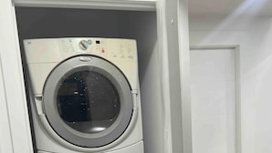 A stacked washer and dryer unit in a room with a wooden floor and white walls. - Room-magnificent Brand New Luxurious Bas (Edmonton)