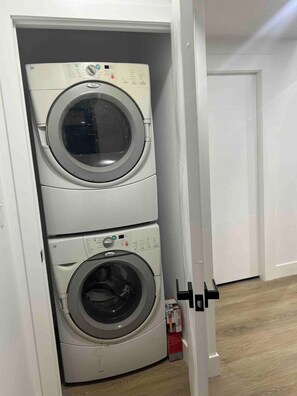 A stacked washer and dryer unit in a room with a wooden floor and white walls.