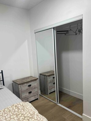 Een slaapkamer met een bed, een houten nachtkastje, een kledingkast met spiegel en een dressoir met lades.