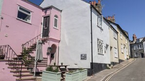 A row of traditional buildings with a pink and white facade, a visible staircase, and outdoor seating area. - 2 Mill Green Court (Lyme Regis)