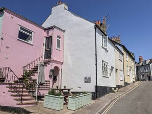 A row of traditional buildings with a pink and white facade, a visible staircase, and outdoor seating area. - 2 Mill Green Court (Lyme Regis)