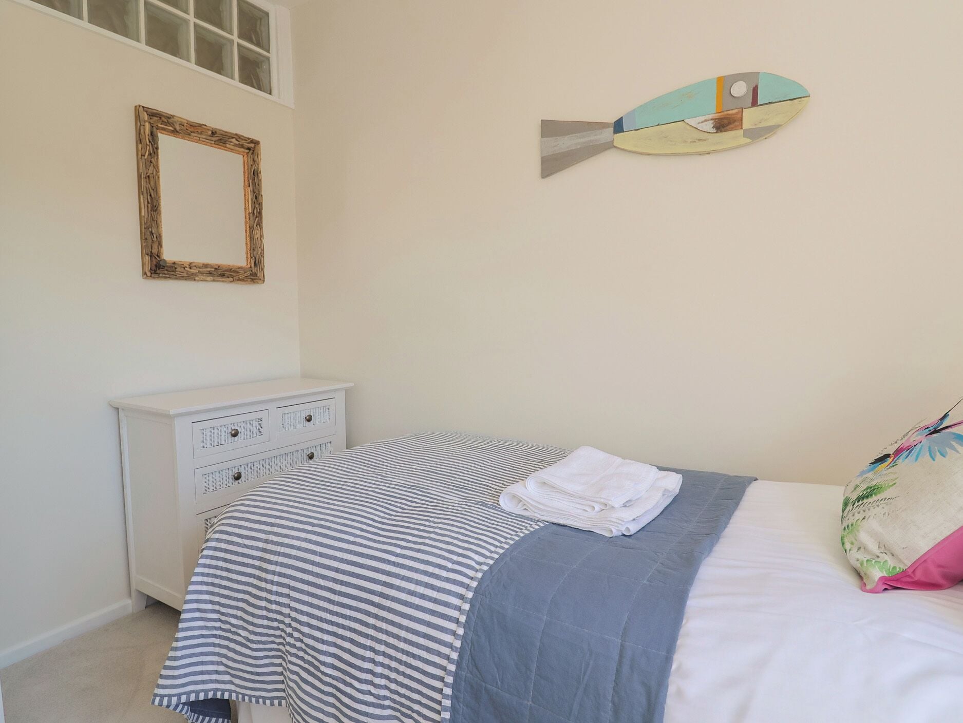 Un dormitorio con cubrecama a rayas, un tocador blanco, un espejo y una pieza de arte de pared con motivo de peces.