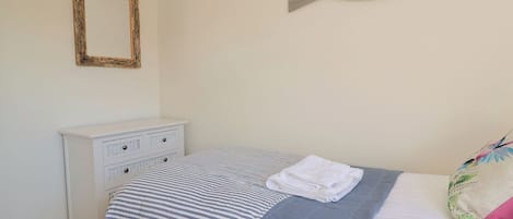 A bedroom with a striped bedspread, a white dresser, a mirror, and a decorative fish wall art piece.