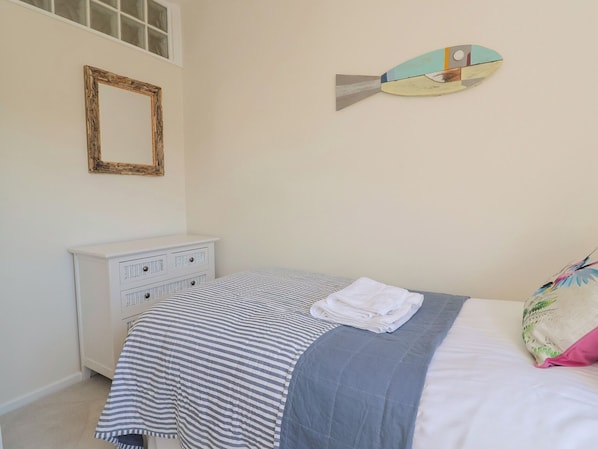 A bedroom with a striped bedspread, a white dresser, a mirror, and a decorative fish wall art piece. - 2 Mill Green Court (Lyme Regis)