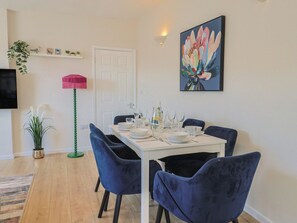 Un comedor con una mesa blanca para cuatro, rodeada de sillas azules, una lámpara de pie y un cuadro en la pared.