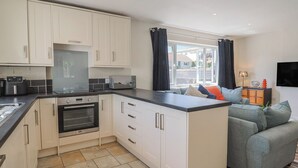 A compact kitchen with white cabinets, a built-in oven, a microwave, and a coffee machine. - 2 Mill Green Court (Lyme Regis)
