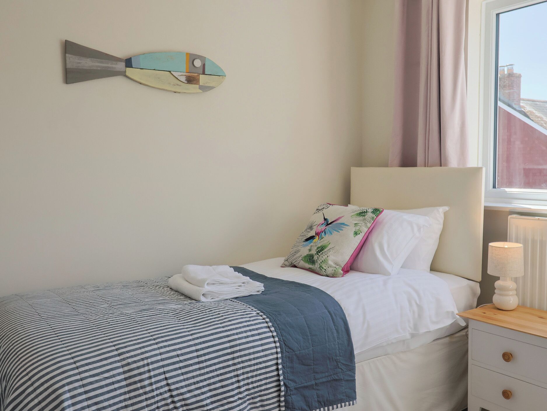 A neatly made bed with a striped blanket, a pillow with a bird print, and a wall-mounted fish decoration.