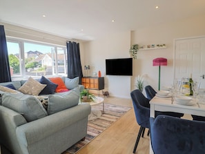 A living room with a sofa, a dining table set with glassware, a flat-screen TV, and a view of the outside. - 2 Mill Green Court (Lyme Regis)