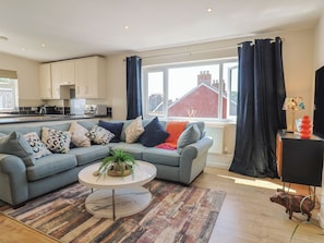 A modern living room with a grey sofa, a round coffee table, and a view of the outside. - 2 Mill Green Court (Lyme Regis)