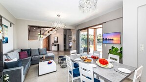 Un soggiorno moderno con un divano grigio, un tavolo da pranzo con sedie, un lampadario e una TV a parete.