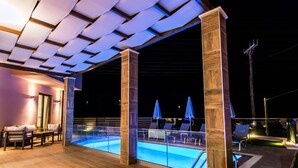 Area piscina all'aperto con lettini e ombrelloni, un pontile in legno e una zona relax coperta con cuscini.