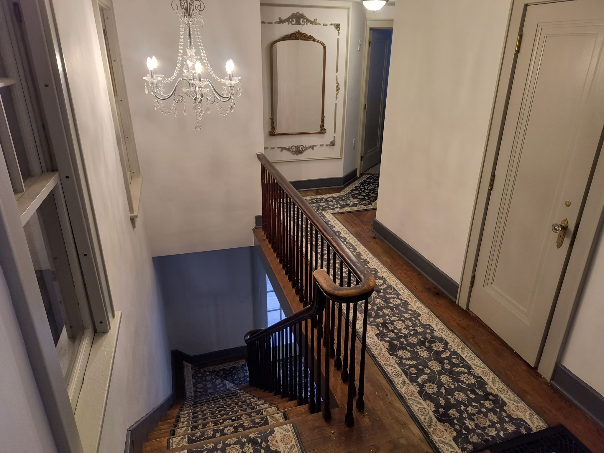 Una escalera con barandilla de madera, alfombra estampada y candelabro.