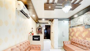A reception area with a sign reading 'TOWNHOUSE,' a white reception desk, two leather sofas, a chandelier, and an air conditioning unit. - Townhouse Rispana Pul Haridwar (Dehradun)