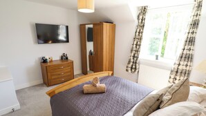 A bedroom with a bed, a wooden wardrobe, a mirror, a television, and a window with curtains. - Burton Fields (Driffield)