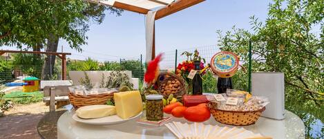 An outdoor dining area with a glass table displaying various food items, a wicker basket, and a decorative fan.