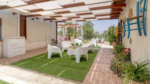 An outdoor patio with white plastic chairs, a small table with a glass, and a pergola with string lights.