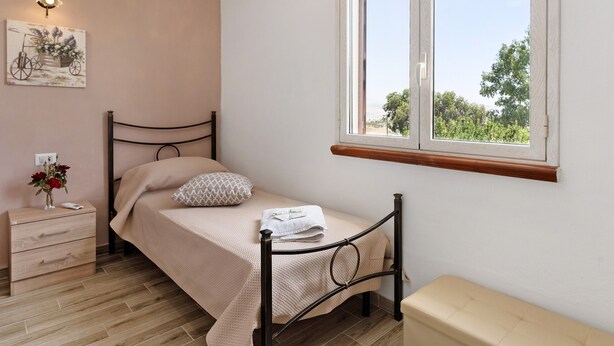 A bedroom with a bed, bedside table, lamp, window, and a wall-mounted picture.