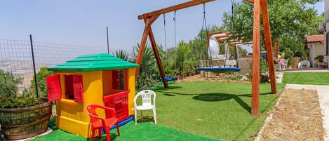 A children's play area with a swing set, a small playhouse, and a green artificial turf.