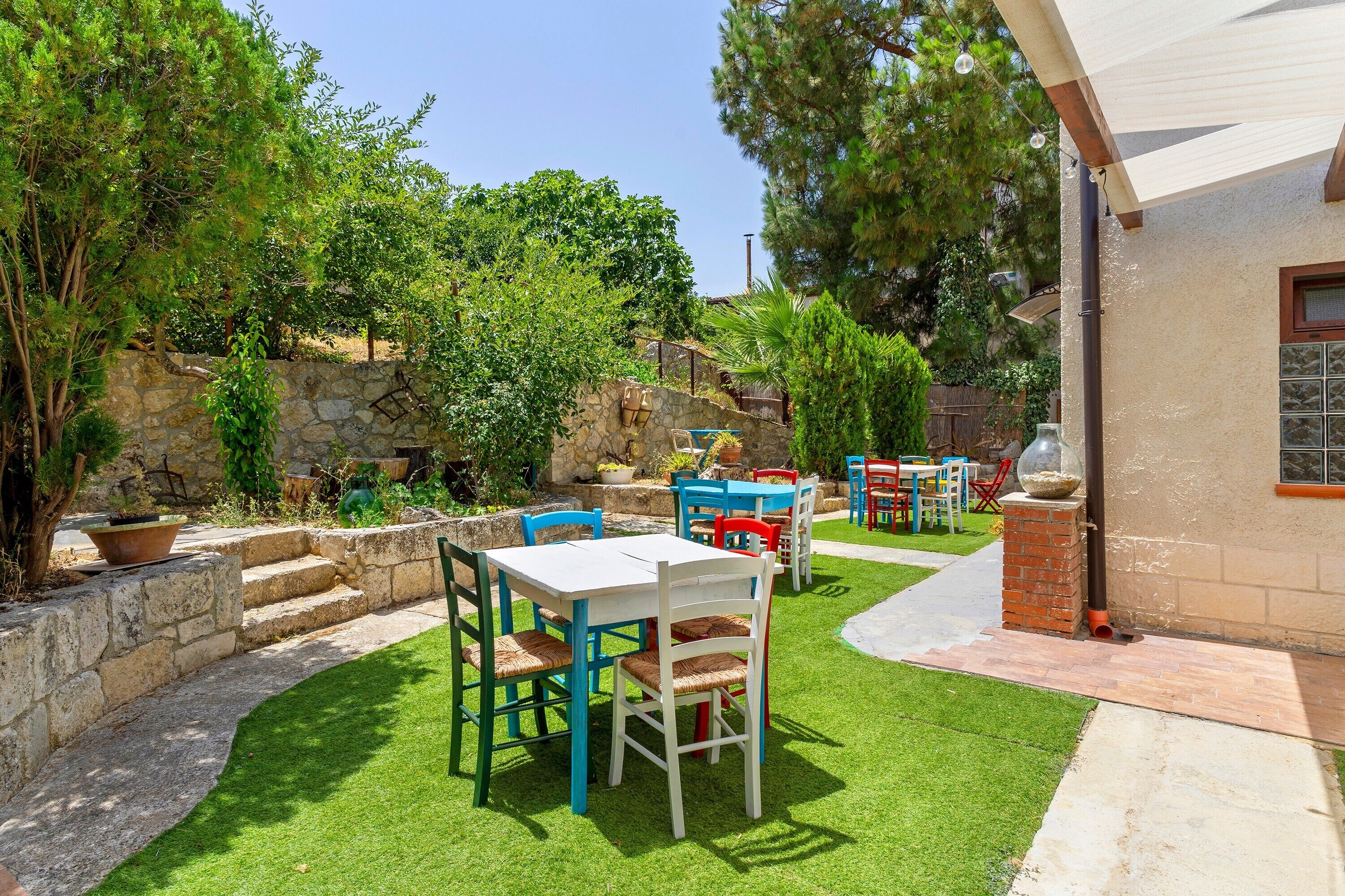 Un patio esterno con un muro in pietra, un prato e diversi mobili da giardino, tra cui tavoli e sedie.