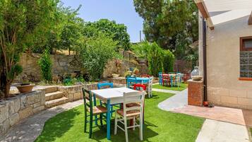Un patio esterno con un muro in pietra, un prato e diversi mobili da giardino, tra cui tavoli e sedie.