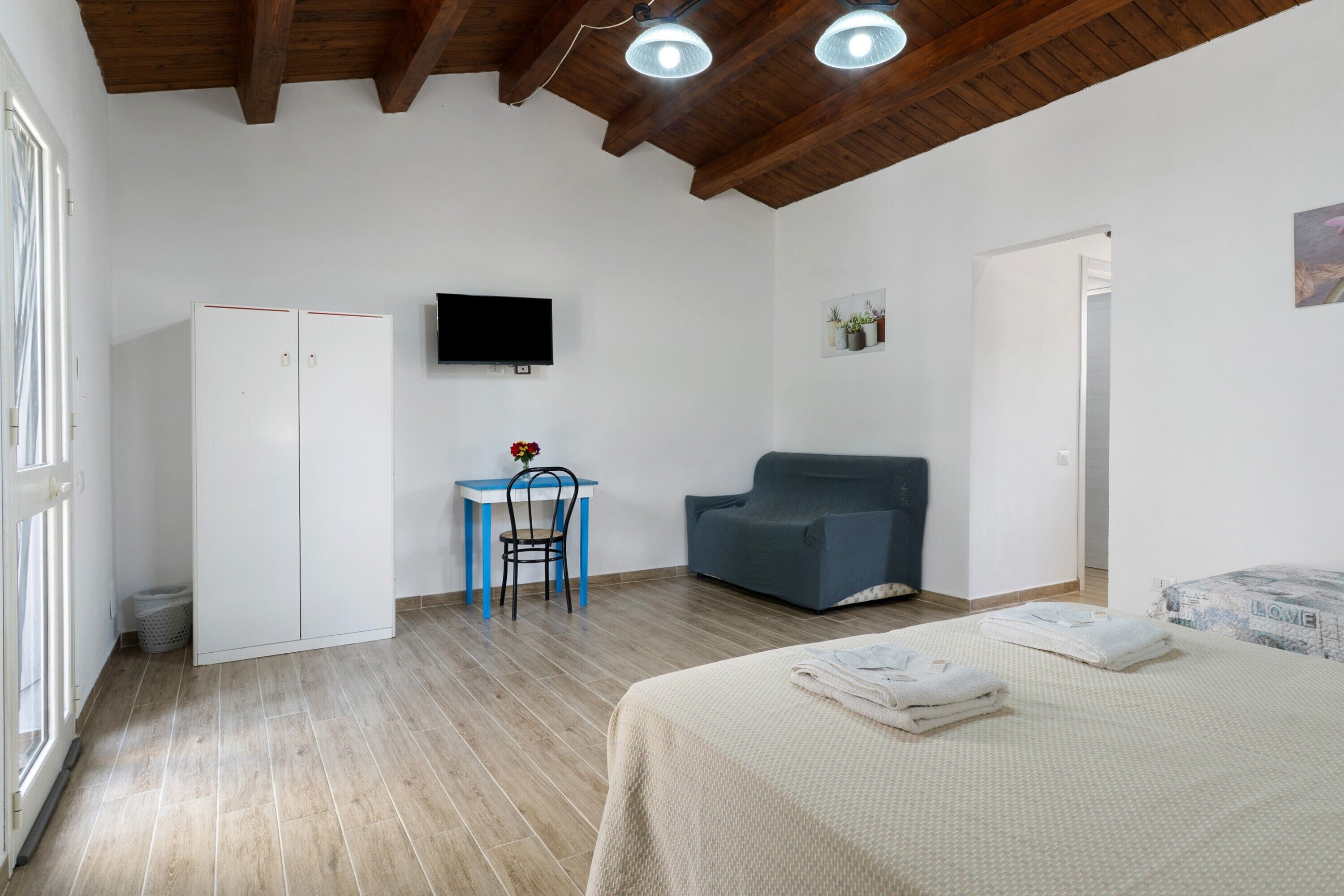 A room with a bed, a desk, a chair, a sofa, a television, and a window.