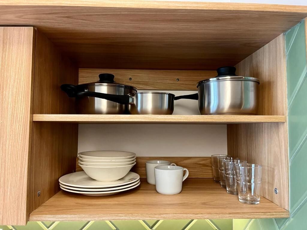 Un armario de madera con estantes que contienen utensilios de cocina, como ollas, platos, una taza y vasos.