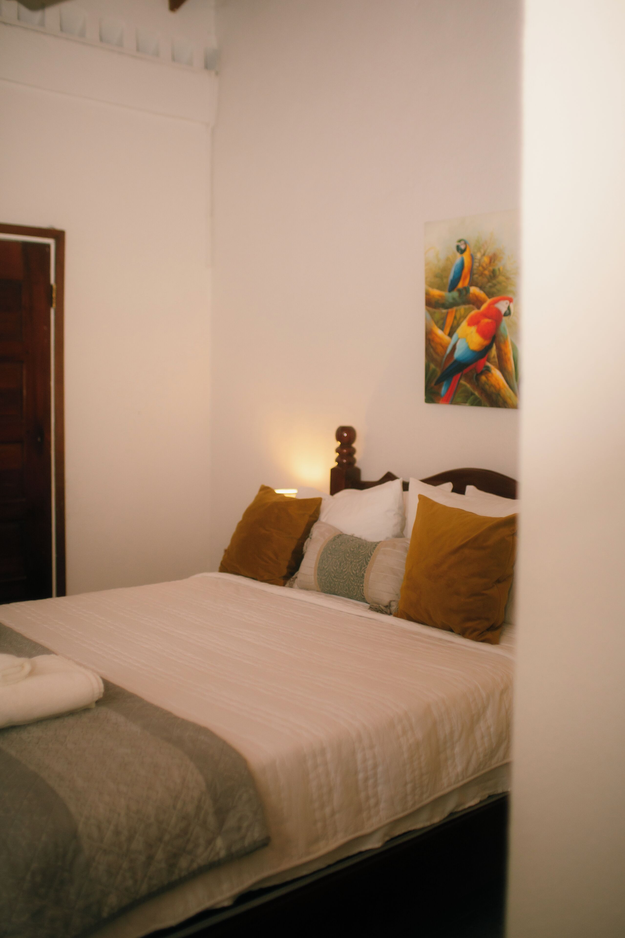 A bedroom with a bed, pillows, a painting, and a door.