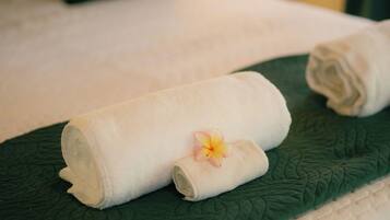 A neatly made bed with a green bedspread, a rolled white towel, and a single flower.