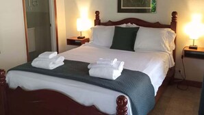 Habitación de hotel con cama, dos lámparas de noche, un cuadro en la pared y una puerta a la izquierda.