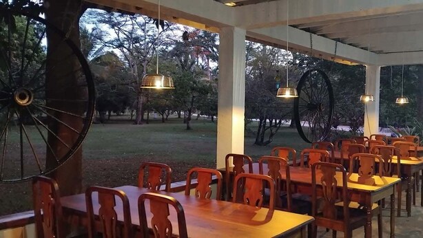 Un espacio para comer al aire libre con mesas y sillas de madera, ruedas grandes como decoración, y luces colgantes.