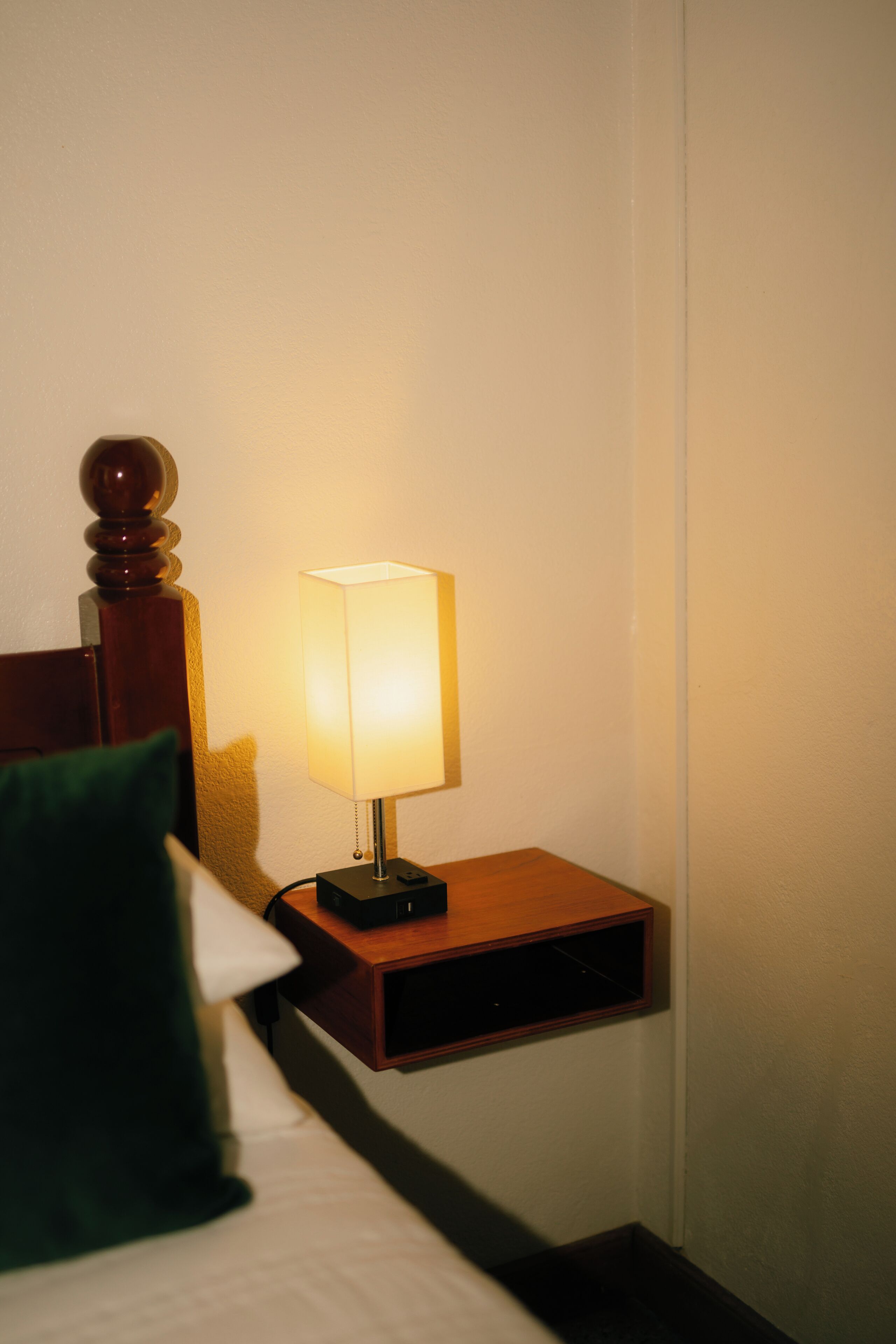 A bed with a green pillow, a bedside table with a lamp, and a wooden headboard.