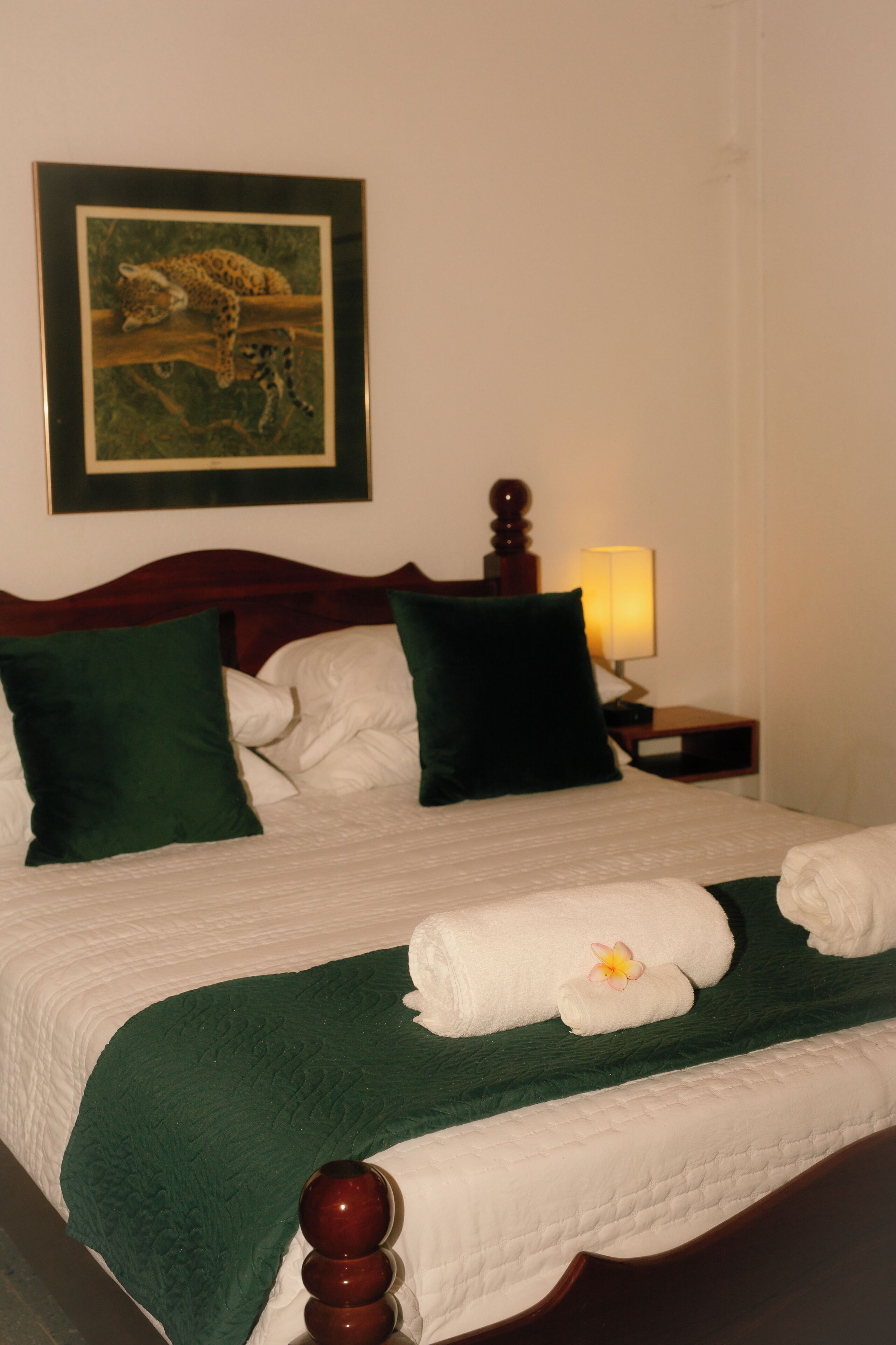 A neatly made bed with a green bedspread, white linens, and a decorative pillow.