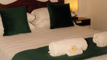 A neatly made bed with a green bedspread, white linens, and a decorative pillow.