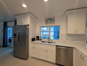 A modern kitchen with white cabinets, stainless steel appliances, and a window providing a view of the outdoors. - Siesta Breeze (Sarasota)